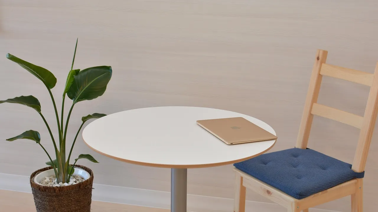 Petite table ronde, un carnet fermé et une chaise vide, avant un entretien.